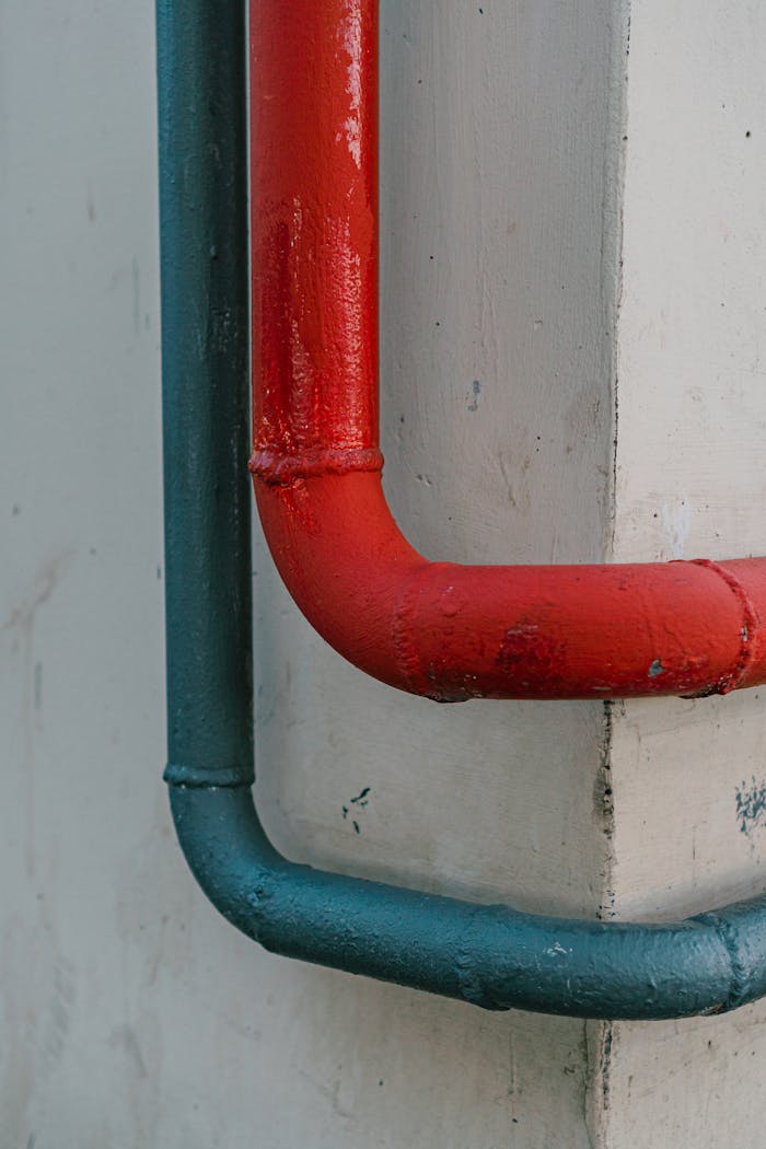 Close-up of vibrant red and blue painted pipes on a textured concrete wall.